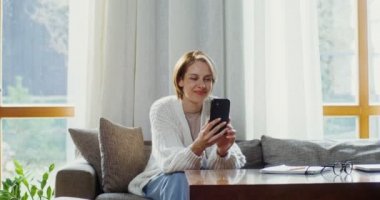 Koltukta otururken cep telefonuyla görüntülü konuşma yapan genç bir kadın.