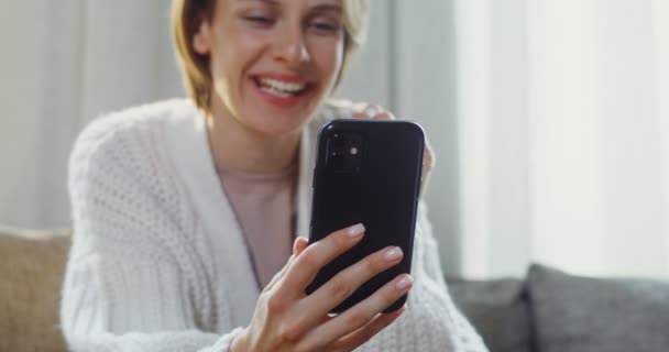 Mladá žena mluví video chat na mobilním telefonu, zatímco sedí na pohovce — Stock video