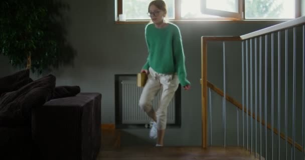 A girl in glasses reading a book with a dreamy look, sitting on the sofa — Stock Video