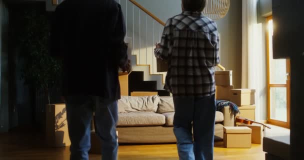 Um homem e uma mulher trazem caixas para dentro de casa, olhando em volta com admiração — Vídeo de Stock