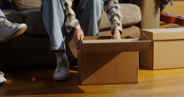 Una mujer está desarmando una caja de libros mientras está sentada en el sofá al lado del hombre — Vídeos de Stock