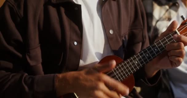 Man speelt de ukelele zittend op de bank naast zijn vrouw tegen de dozen — Stockvideo