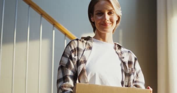 Una joven está sonriendo mirando a la cámara y sosteniendo una caja en sus manos — Vídeos de Stock