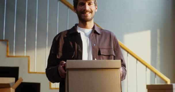 Un hombre sonríe mientras mira a la cámara y sostiene una caja en sus manos — Vídeos de Stock