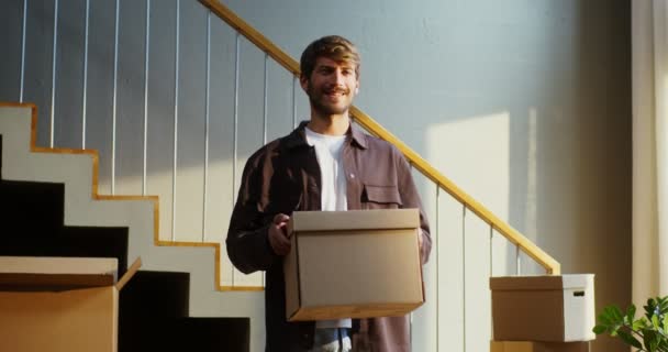 Egy férfi mosolyog, miközben a kamerába néz és egy dobozt tart a kezében. — Stock videók
