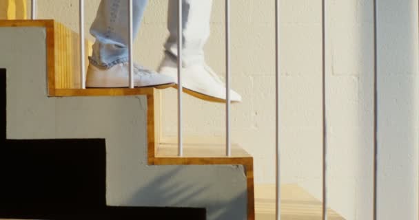Muž sejde ze schodů, nohy v bílých teniskách a džínách zblízka — Stock video