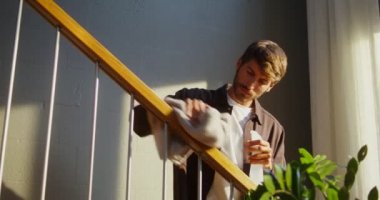 Bir adam merdivenlerin korkuluklarını yıkıyor, pultilizerden sıvı püskürtüyor.