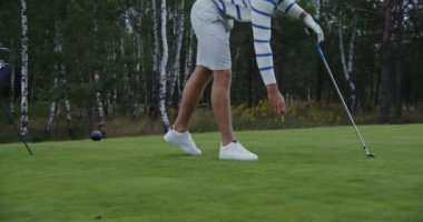 Genç bir adam golf topunu yere saplar ve üzerine bir golf topu koyar.