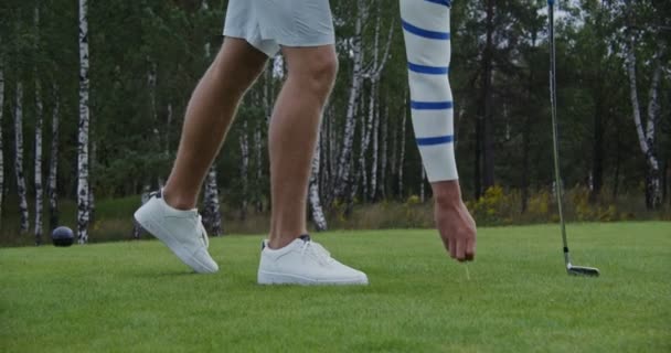 En man sticker en tee i marken och placerar en golfboll på den — Stockvideo