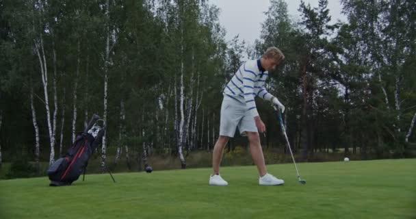 Mladý muž strčí držák golfového míčku do země a položí na něj golfový míček — Stock video