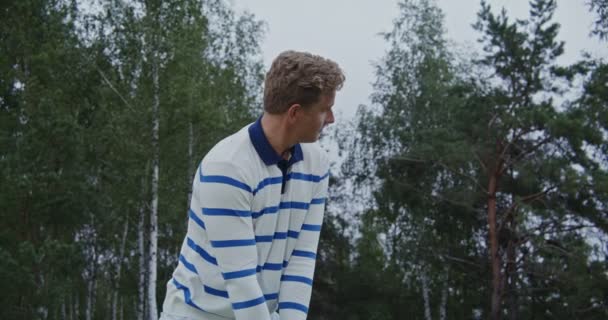Genç bir adam topa golf sopasıyla vurmaya hazırlanıyor, mesafeyi gözetliyor. — Stok video