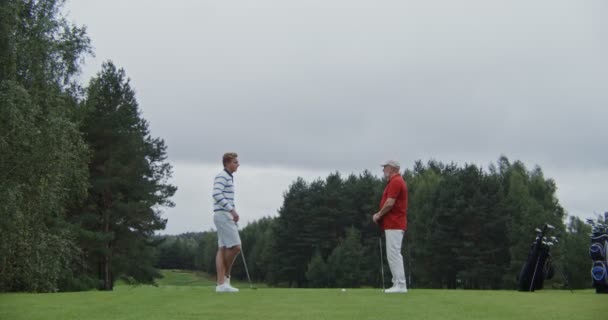 Двоє стильно одягнених чоловіків з чудовим віковим розривом балачки і грати в гольф разом — стокове відео