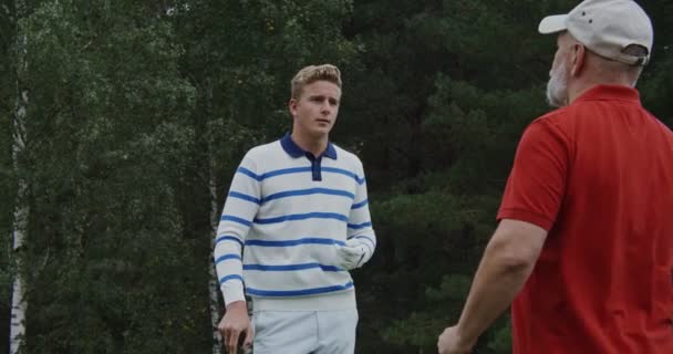 Giovane uomo con una mazza da golf in mano comunica con l'uomo anziano all'aperto — Video Stock