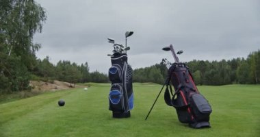 Golf sopalarıyla dolu golf çantaları manikürlü bir golf sahasında duruyor.