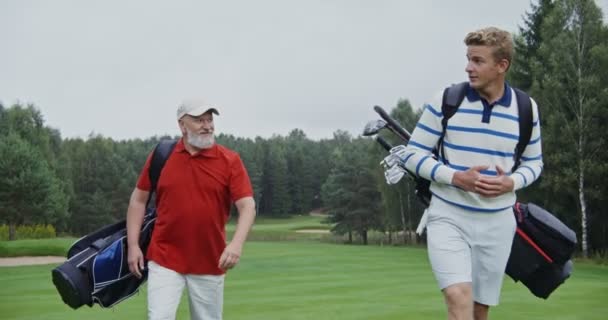 Dos hombres van a jugar golf en un césped bellamente recortado en un día soleado — Vídeo de stock