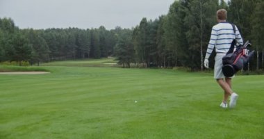 Adamın biri golf topuna doğru yürür bir golf sopası kapar ve bir sonraki vuruşu yapar.