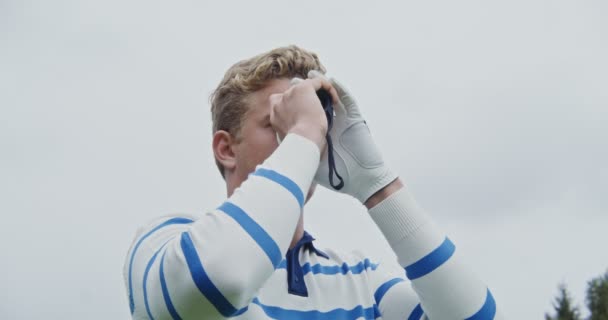 A young man in a white golf glove peers through binoculars in search of a hole — Stock Video