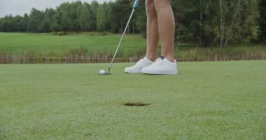 Adamın biri golf sopasıyla topa vuruyor ve yakın plan bir deliğe vuruyor.