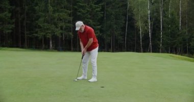 Bir adam golf oynuyor, golf sopasıyla golf topuna vuruyor ve topu deliğe sokuyor.