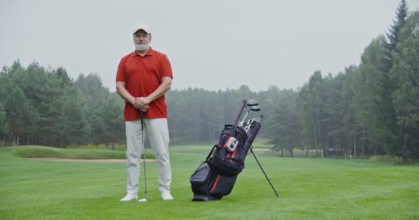 Um homem idoso com stands em um campo de golfe, apoiando-se em um clube de golfe — Vídeo de Stock