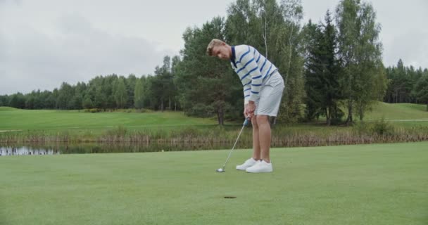 Egy fiatalember lassan a lyukba dobja a golflabdát, és golfütővel üti. — Stock videók