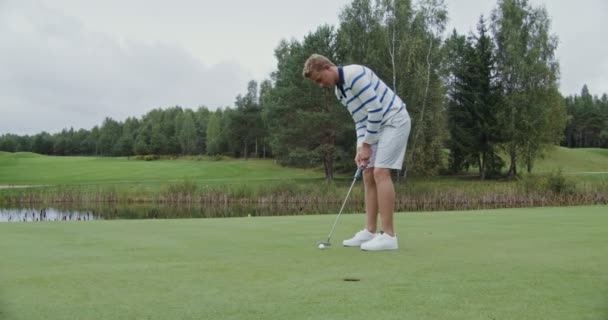 Un homme lance une balle de golf dans le trou, la frappe avec un club, mais manque — Video