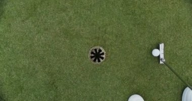 Adamın biri golf sopasıyla topa vuruyor ve top hedefi vuruyor.