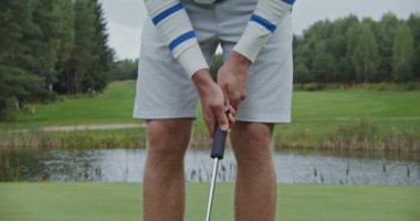 Yere eğilmiş bir adam elinde golf sopasıyla golf topuna vuruyor.