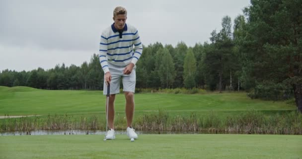 Um jovem aponta e acerta uma bola com um taco de golfe, mas falha — Vídeo de Stock