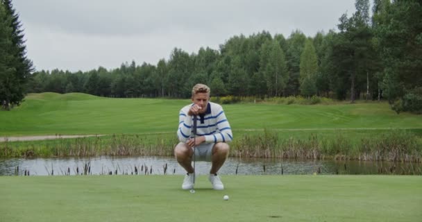 En man tar sikte och slår bollen med en golfklubba och kör den in i hålet — Stockvideo
