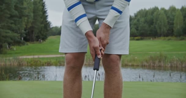 Een man die naar de grond leunt, houdt een golfclub in zijn handen en slaat een golfbal. — Stockvideo