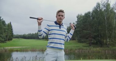 Bir adam kafasının arkasında golf sopası tutarken kameraya bakarken gülümsüyor.