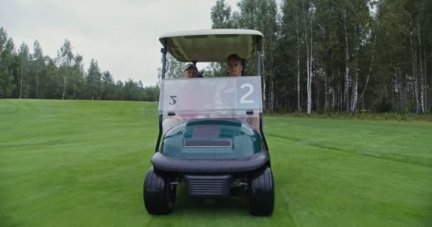 Dois homens estão dirigindo um carro de golfe em um campo de golfe e conversando uns com os outros — Vídeo de Stock