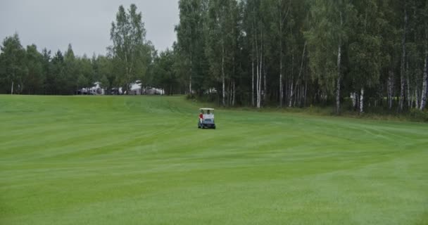 Vista panorâmica do campo de golfe com o carro de golfe que o atravessa — Vídeo de Stock