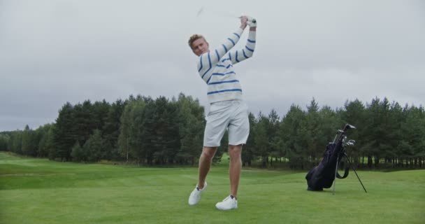 Anak muda berayun dan memukul bola secara paksa dengan tongkat golf — Stok Video