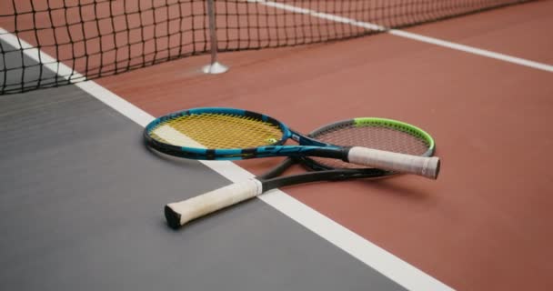 Två tennisracketar ligger på golvet nära spelnätet. — Stockvideo