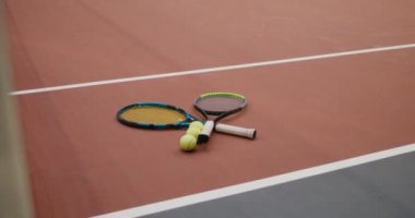 Tenis raketleri ve tenis topları tenis ağının yanındaki kauçuk zeminde yatıyor.
