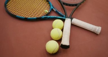 Tenis kortunda tenis raketinin yanında üç tenis topu yatıyor.