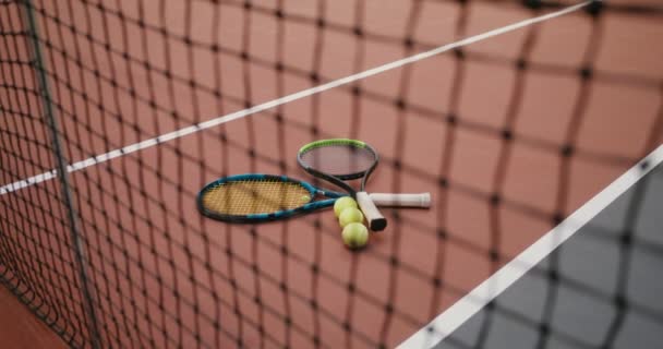 Two tennis rackets with three tennis balls lie on tennis field near tennis net — Stock Video