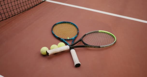 Raquetas de tenis se encuentran uno a uno en la pista de tenis al lado de pelotas de tenis — Vídeos de Stock