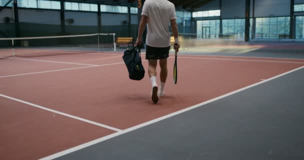 Az ember besétál a teniszpályára egy ütővel és egy zacskó cuccal, és játszani megy. — Stock videók