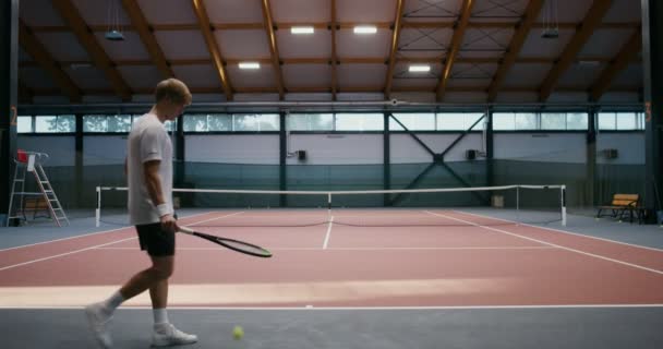 Un uomo che colpisce la palla da tennis dal pavimento con una racchetta e colpisce la palla sopra la rete — Video Stock