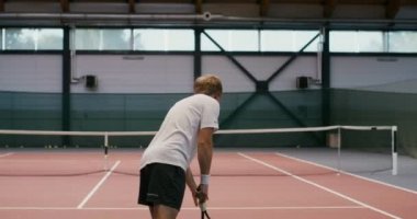 Tek başına tenis oynayan bir adam, kaleye tenis topu atıyor.