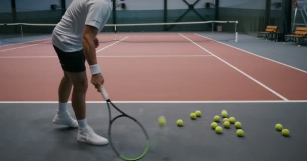 Egy férfi sok teniszlabdát készített a földön, és lármával emelte fel őket. — Stock videók