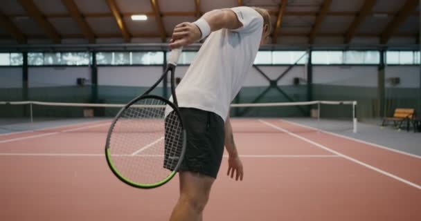 Мужчина бросает теннисный мяч с ракеткой через сетку, видео со спины — стоковое видео