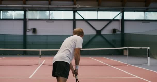 En man spelar tennis ensam, kastar tennisbollar över nätet — Stockvideo