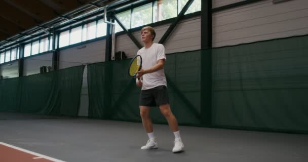 Een man speelt tennis, slaat bal voor bal met een racket, indoor spelen — Stockvideo