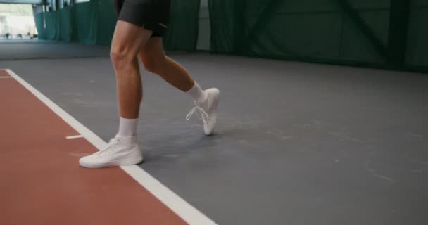Мужчина играет в теннис, бьет по мячу ракеткой, играет в помещении — стоковое видео