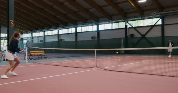 Joven hombre y mujer juegan al tenis, lanzando la pelota con raquetas sobre una red — Vídeos de Stock