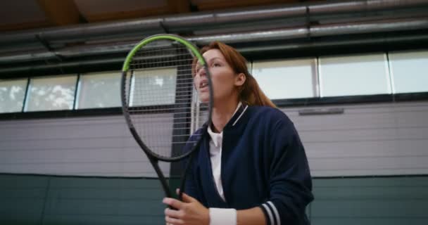 Młoda piękna kobieta uderza piłkę tenisową rakietą, rzucając nią przez siatkę — Wideo stockowe